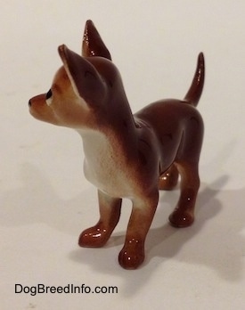 The front left side of a brown with white Chihuahua figurine. The figurine has a prominent chest.